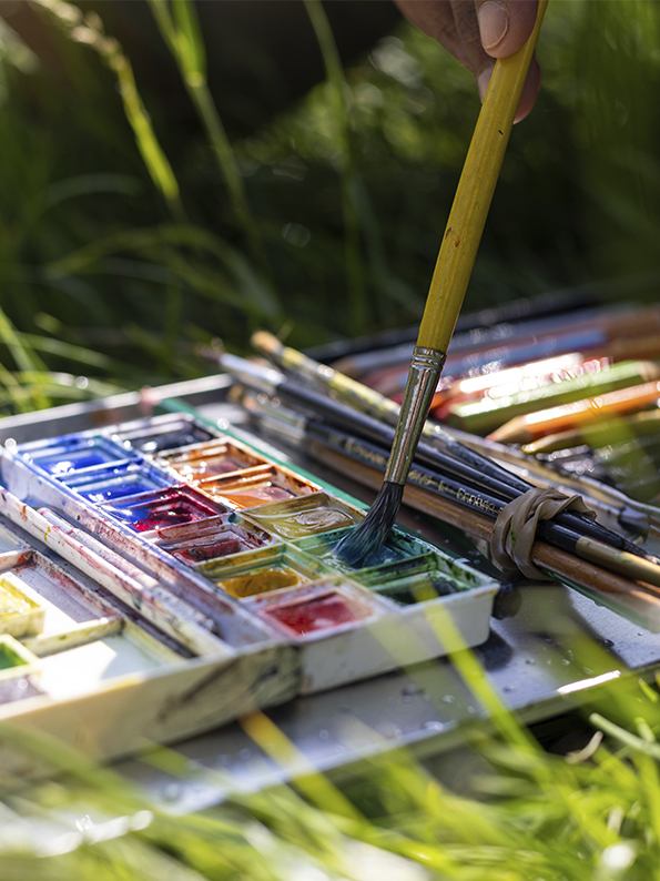 Ein Farbkasten mit Pinseln auf einer Wiese.Foto: SolStock via iStock