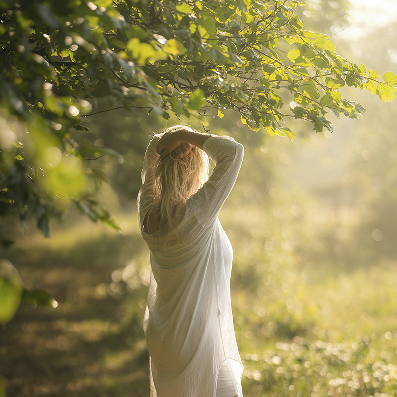 Rückansicht einer Frau die an einem See steht und die Arme über den Kopf streckt.Foto: Christopher Campbell via Unsplash