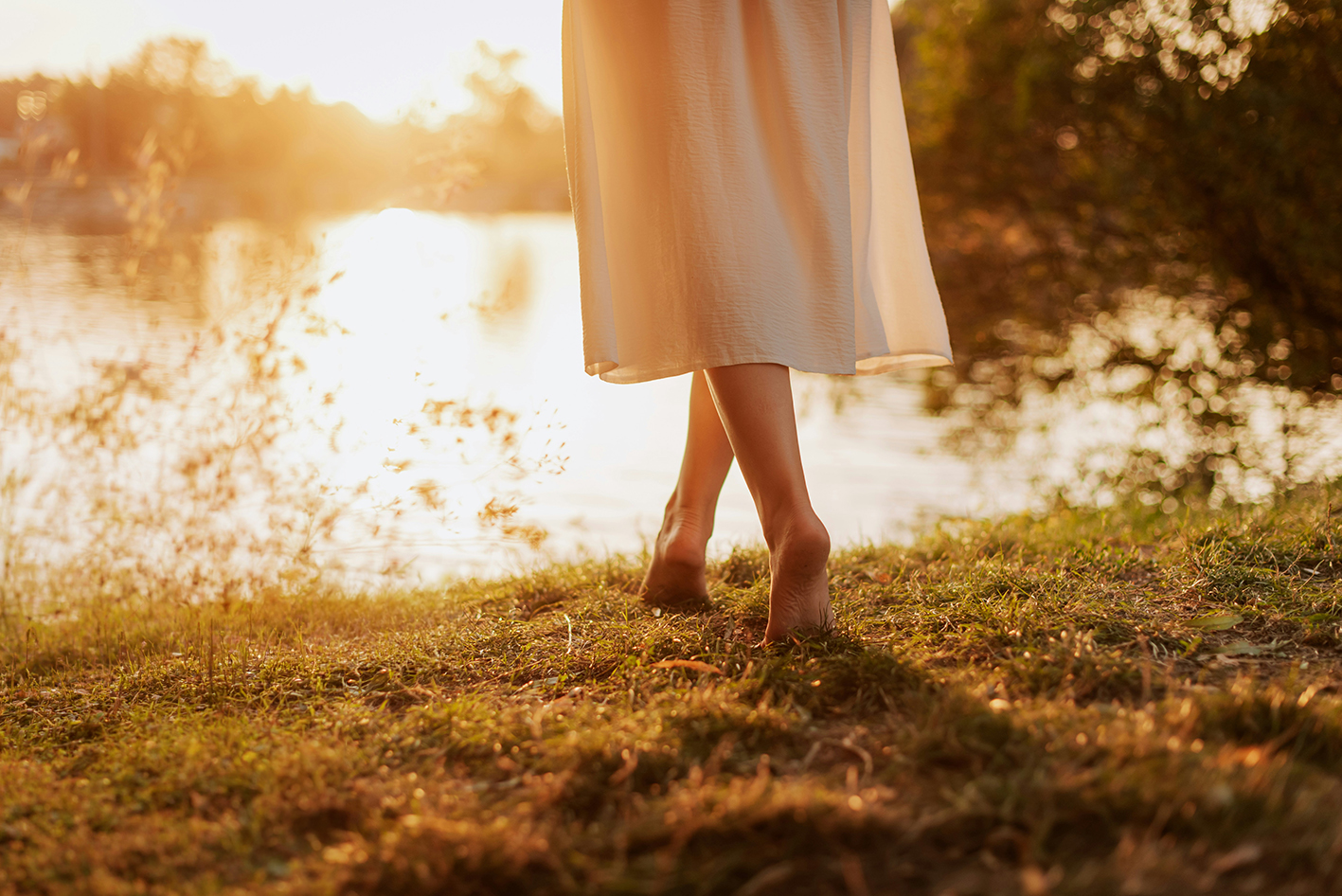 Ein Frau läuft im Sonnenaufgang barfuß auf ein Seeufer zu.