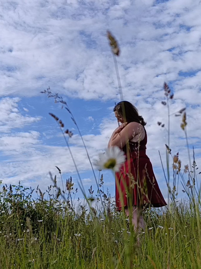 Tess steht auf einer Blumenwiese und hält sich selbst.