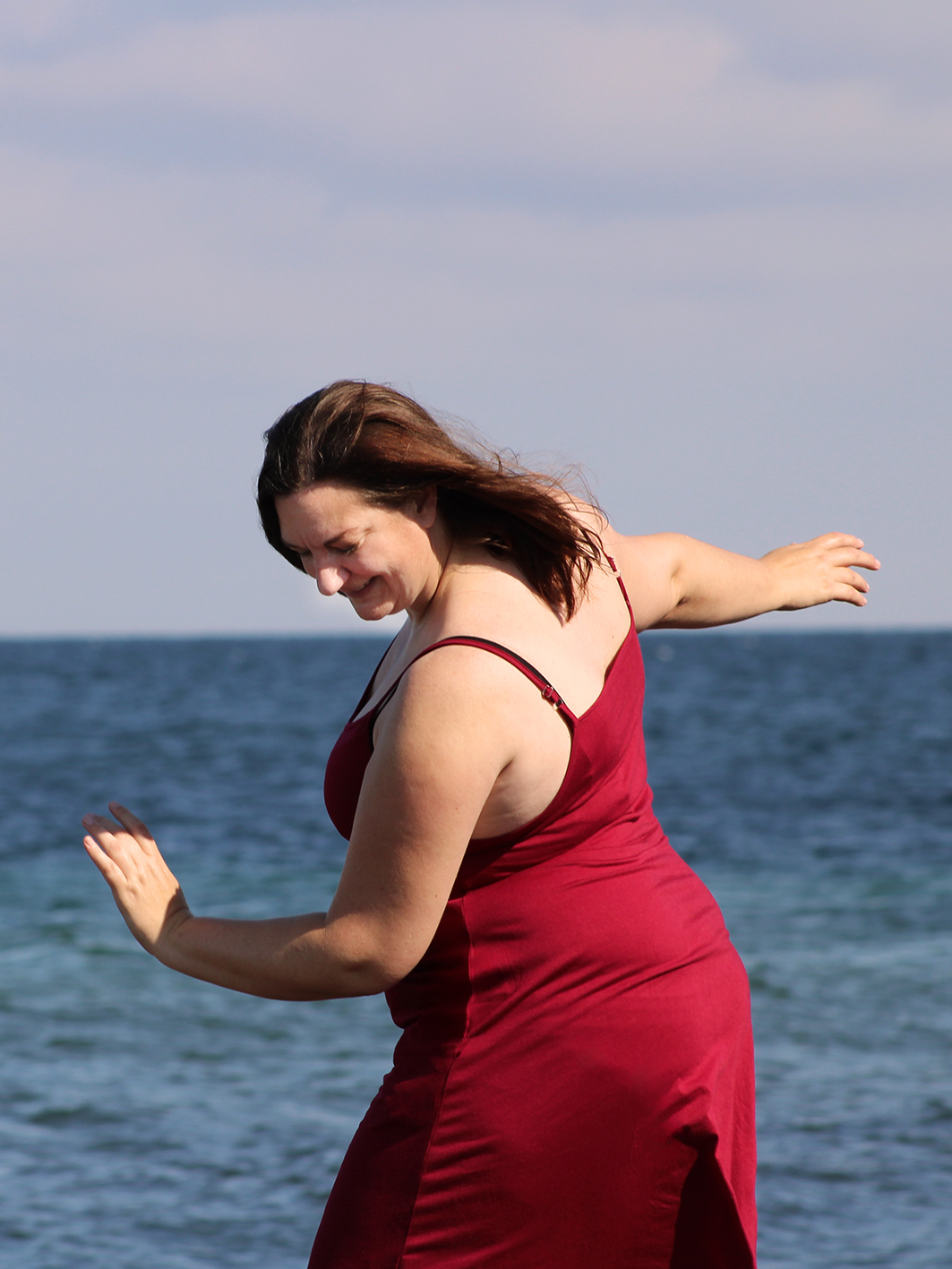 Tess tanzt in einem roten Kleid vor der dunkelblauen Ostsee.